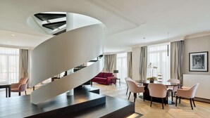 Un interior moderno con una escalera espiral, un comedor y una sala de estar con un sofá rojo y una araña.