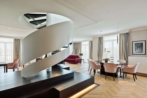 Un interno moderno con una scala a chiocciola, una zona pranzo e un soggiorno con un divano rosso e un lampadario.