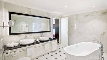 A modern bathroom with a large mirror, two sinks, a bathtub, and a toilet.
