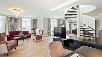 A modern living room with a curved staircase, a flat-screen TV, and plush seating.
