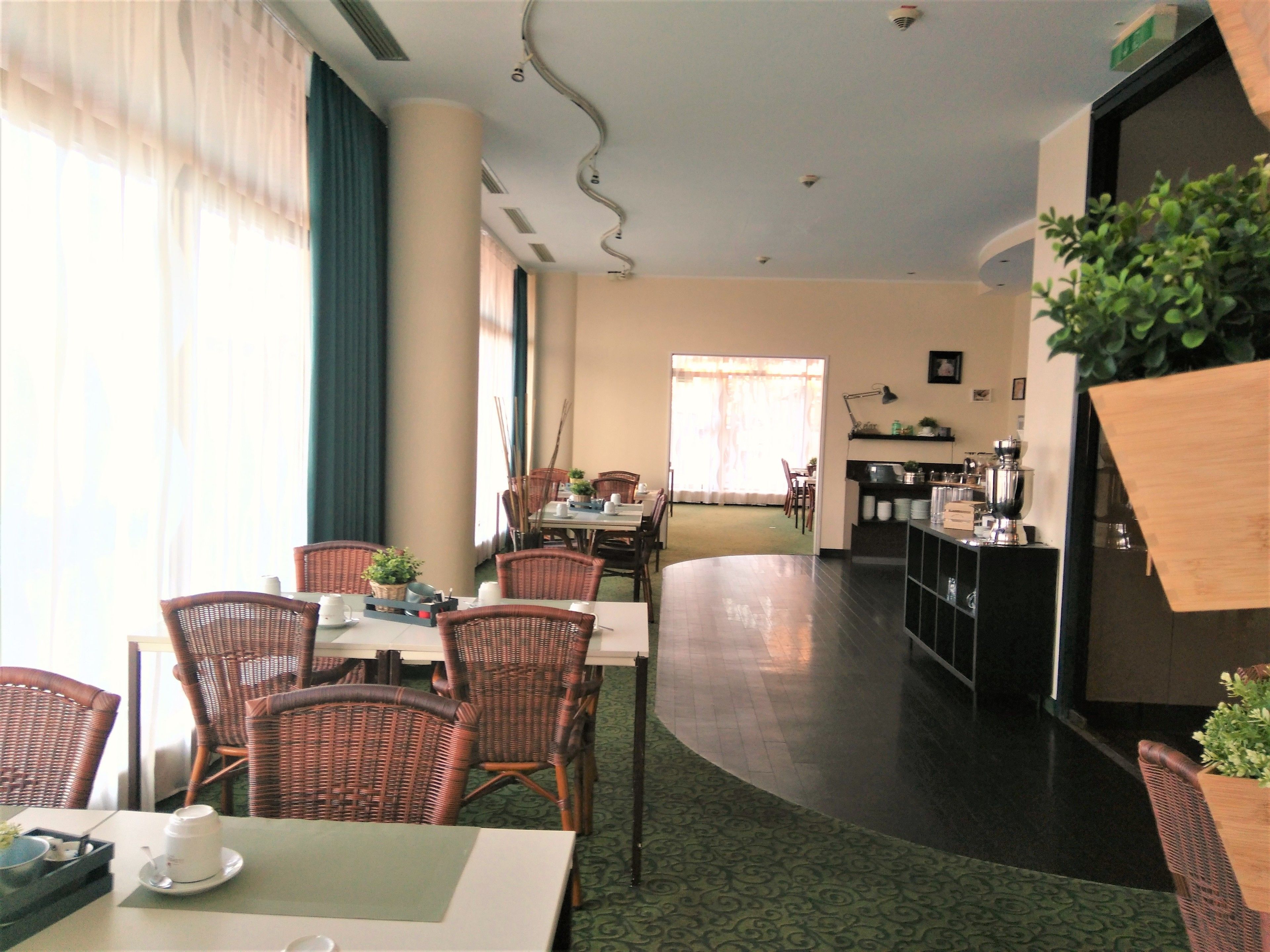 A dining area with wicker chairs and a table, a kitchen area with appliances, and a view of the outdoors through large windows.