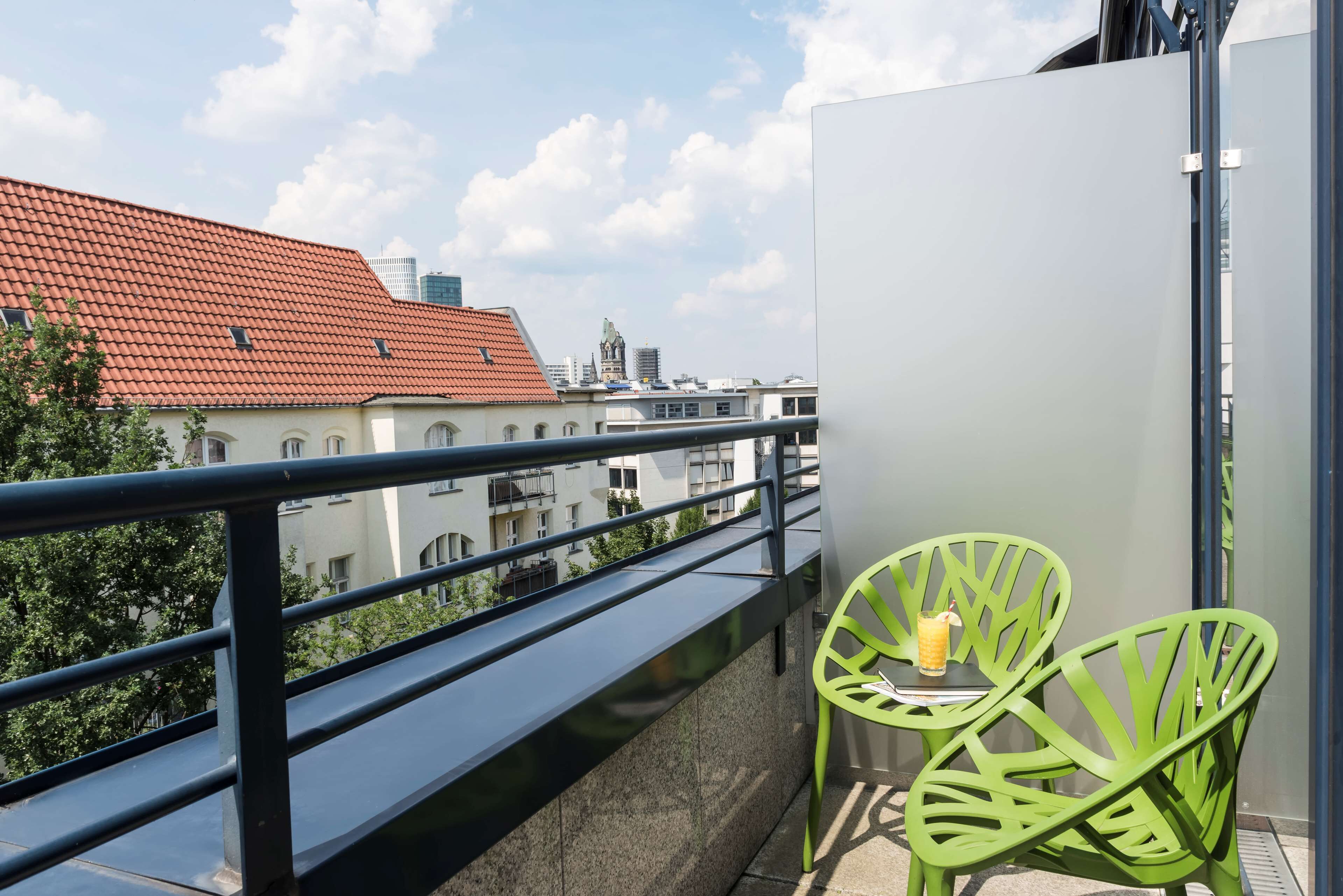 A balcony with a metal railing, two green chairs, and a table with a glass of juice.