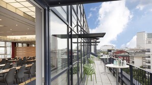 A modern hotel interior with a dining area, a balcony with tables and chairs, and a city view. - Scandic Berlin Kurfürstendamm (Berlin)