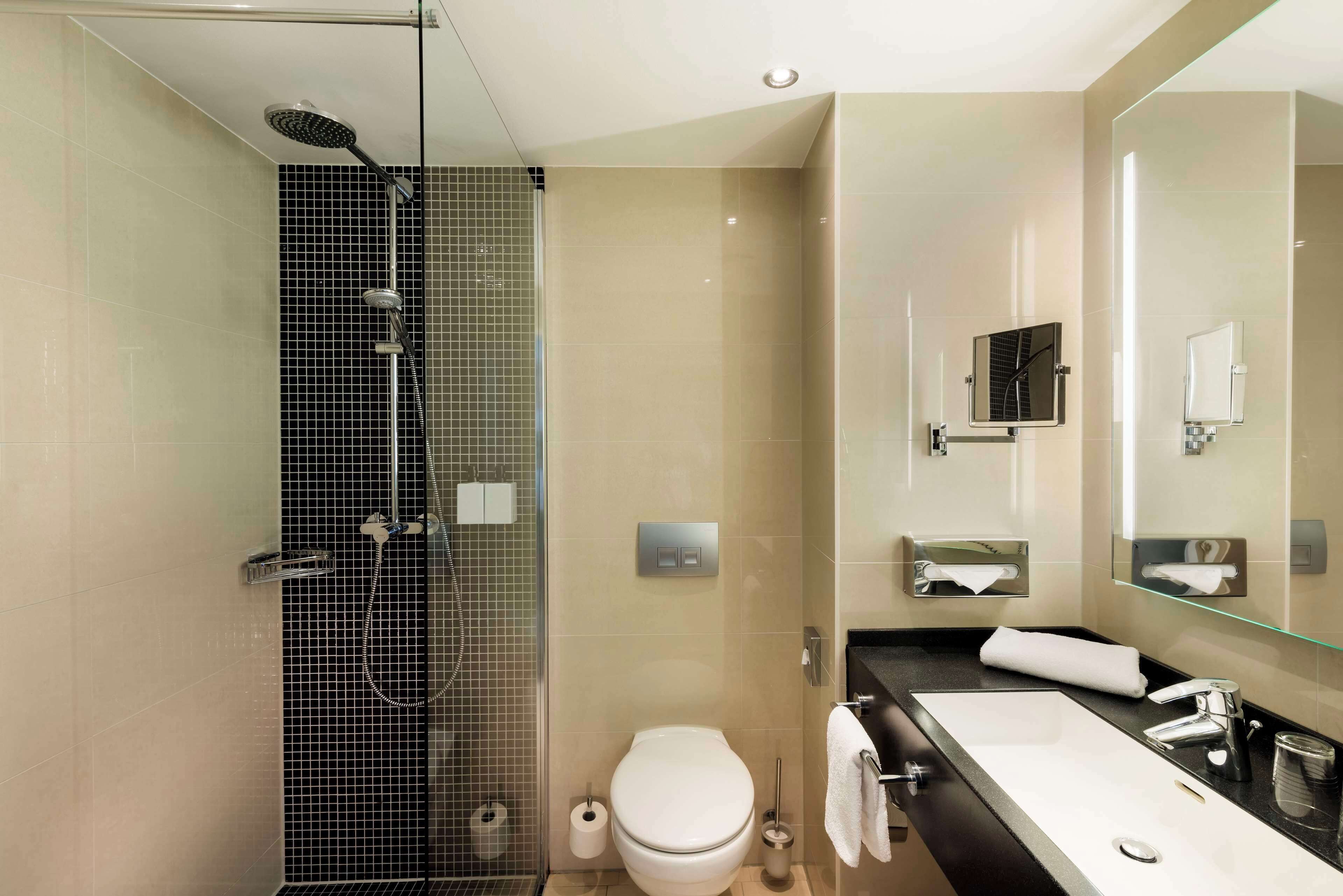 A modern bathroom with a glass-enclosed shower, a white toilet, a large sink with a mirror, and a towel rack.