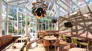 A spacious indoor area with large windows, multiple seating arrangements, and a unique ceiling light fixture. - Scandic Berlin Kurfürstendamm (Berlin)