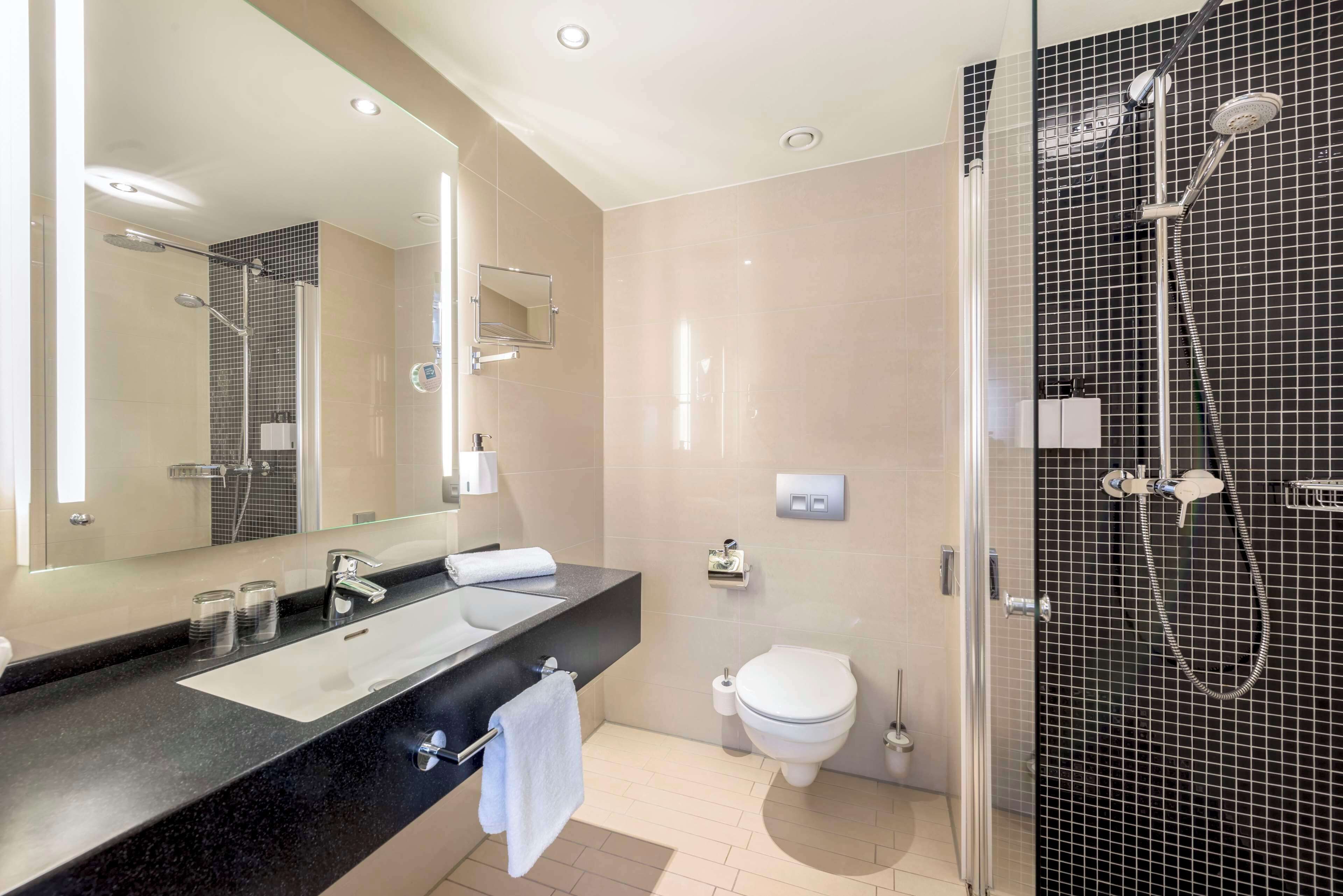Un baño moderno con un espejo grande, un lavamanos, un inodoro y una zona de ducha.