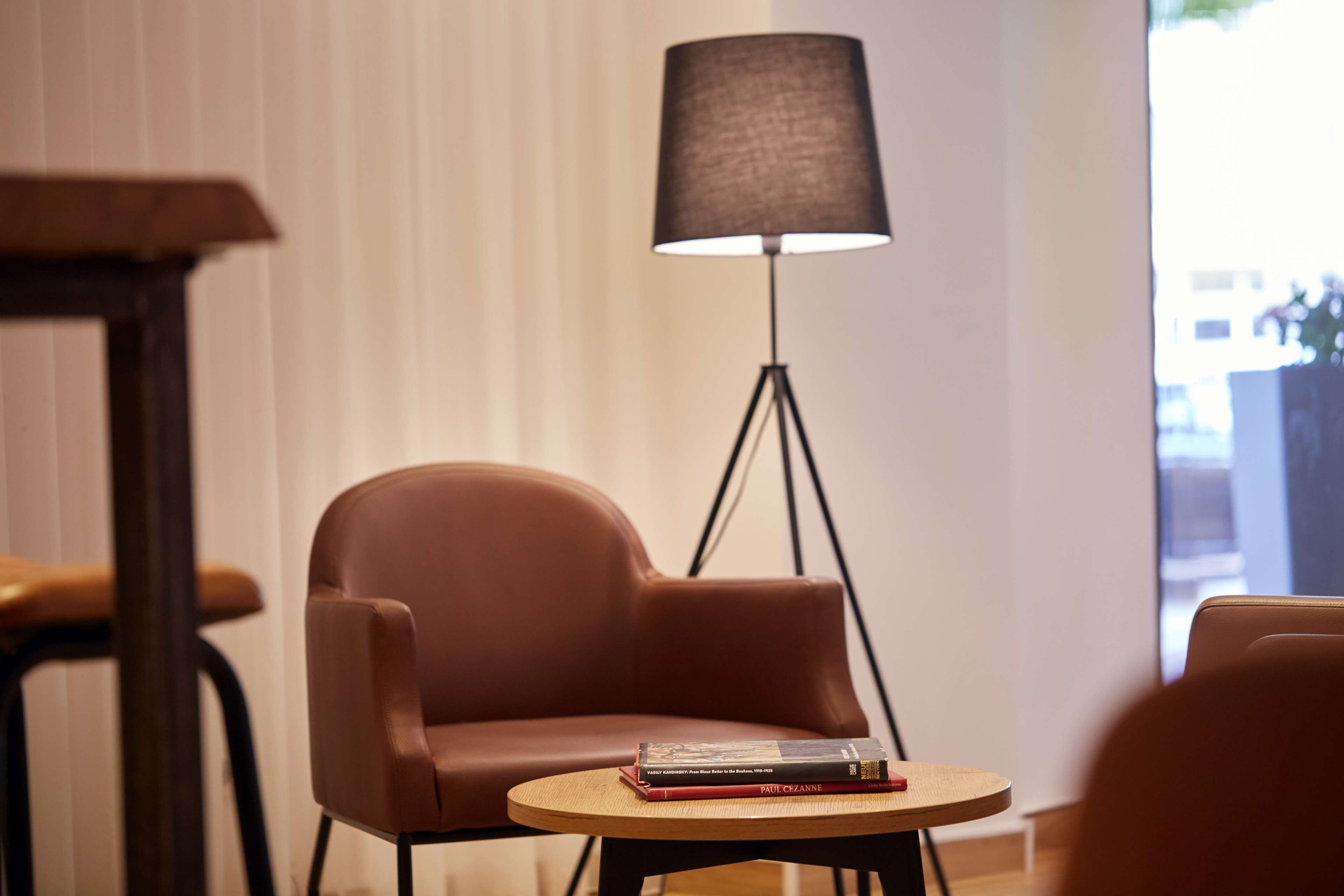 Une pièce moderne avec un fauteuil en cuir marron, une petite table en bois sur laquelle sont posés des livres et un lampadaire.