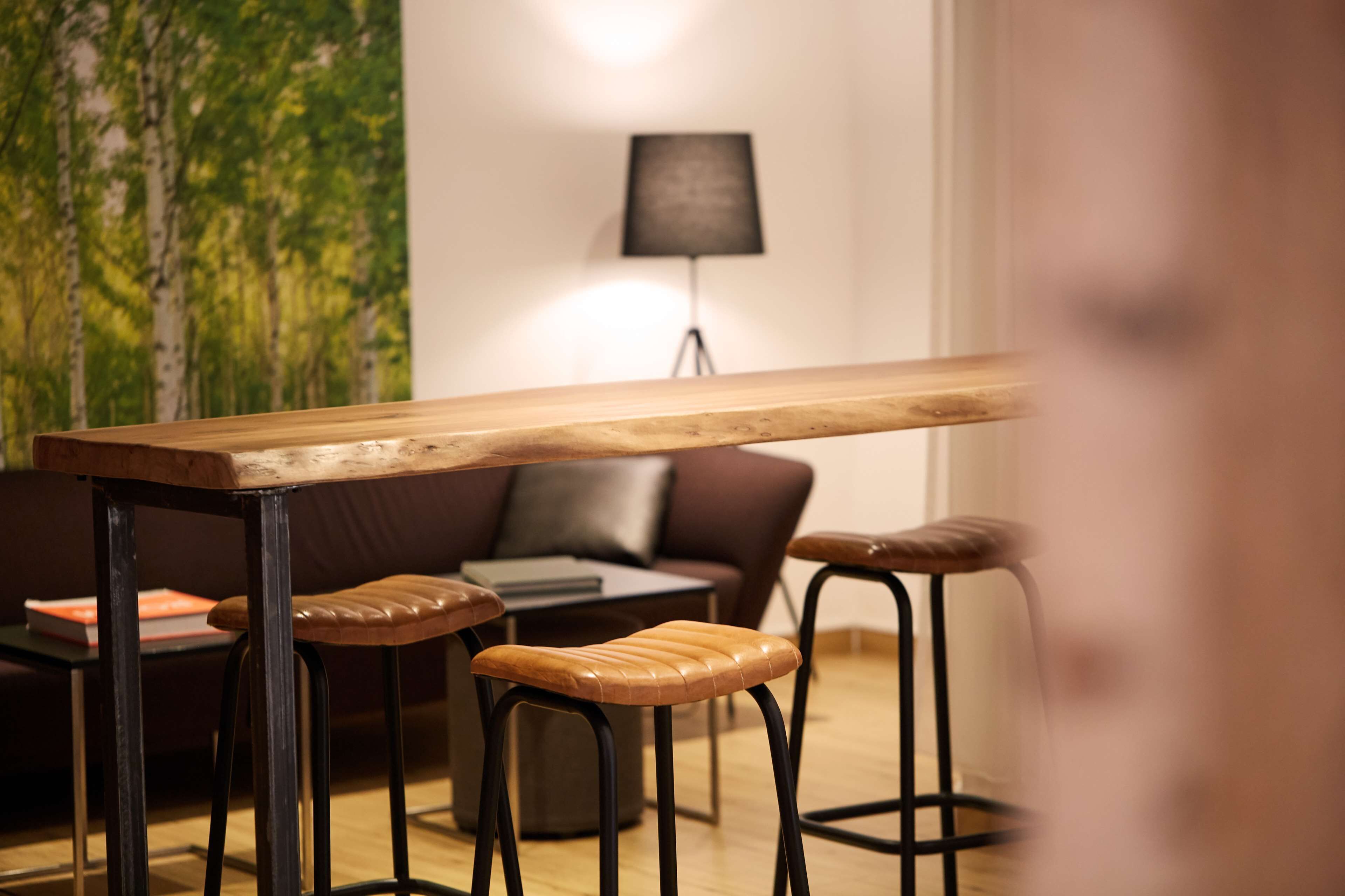 Un interior moderno con una mesa de madera, taburetes de bar de cuero, un sofá de cuero marrón y una lámpara.