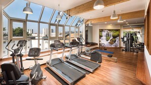A gym with treadmills, elliptical machines, and weight equipment. Large windows offer views of the city. - Scandic Berlin Kurfürstendamm (Berlin)