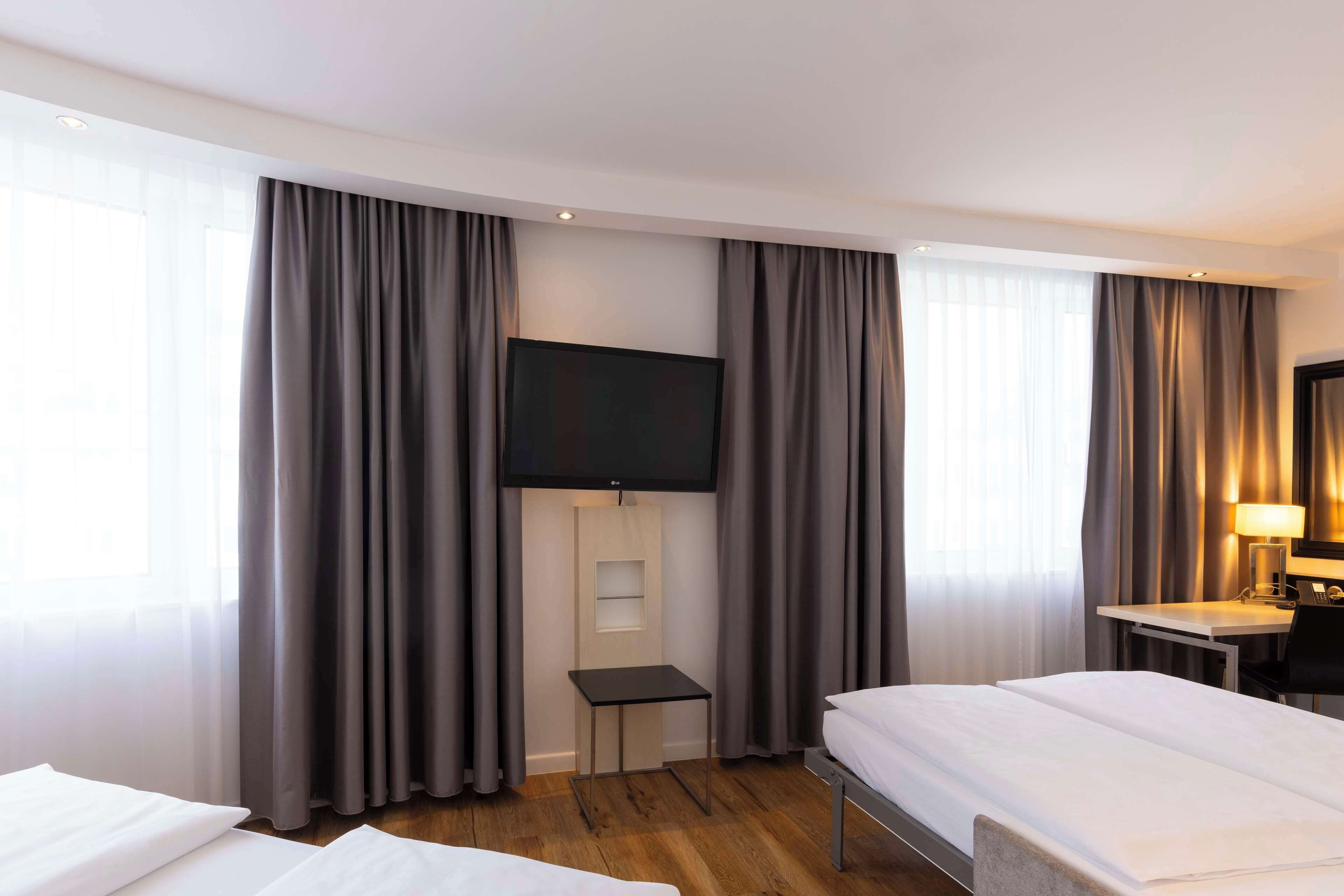 Habitación de hotel con dos camas, un televisor, un escritorio con lámpara y una mesita pequeña.