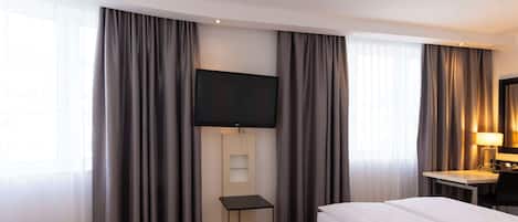 A hotel room with two beds, a TV, a desk with a lamp, and a small table.