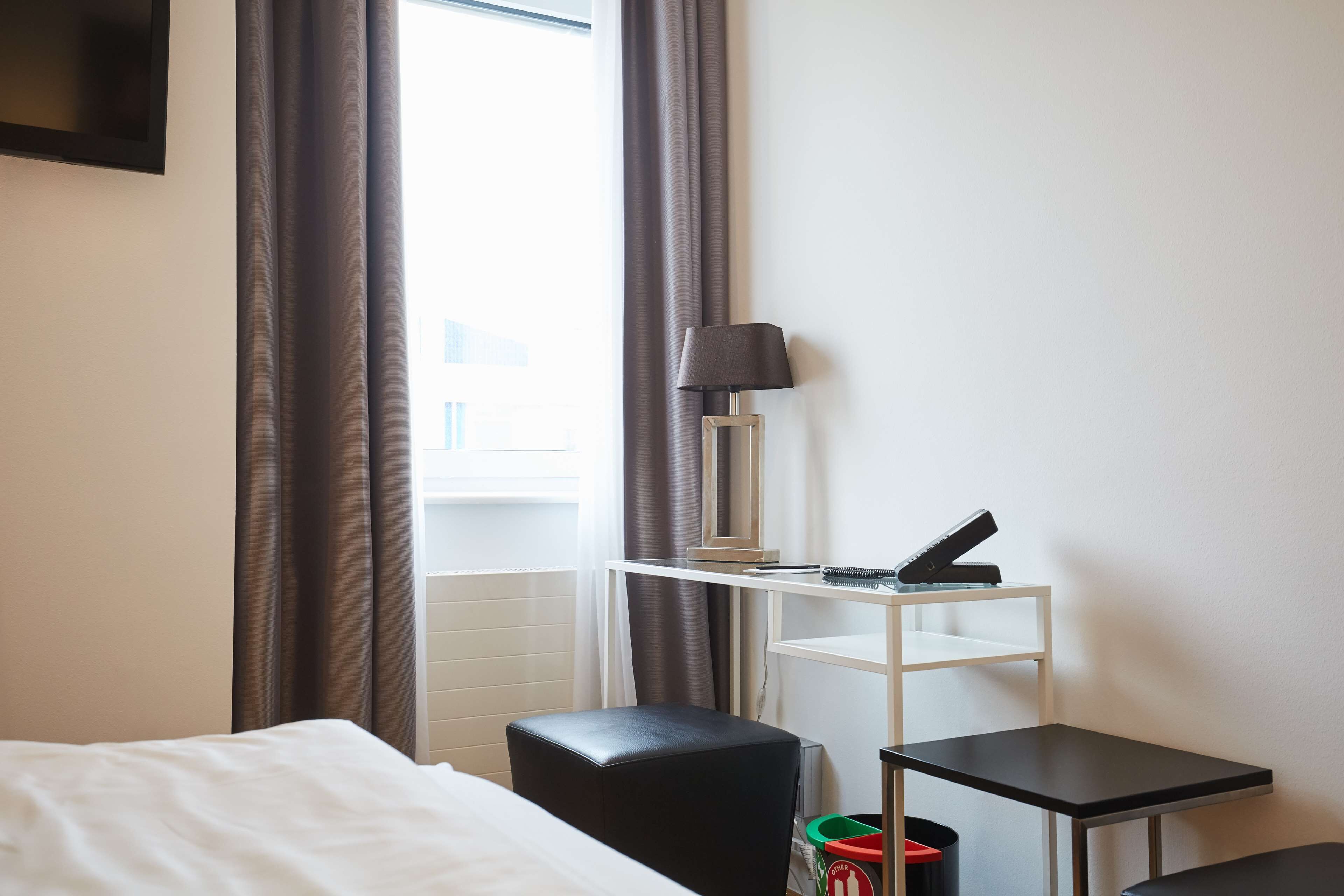 A hotel room with a bed, a desk with a lamp, a chair, and a small table.