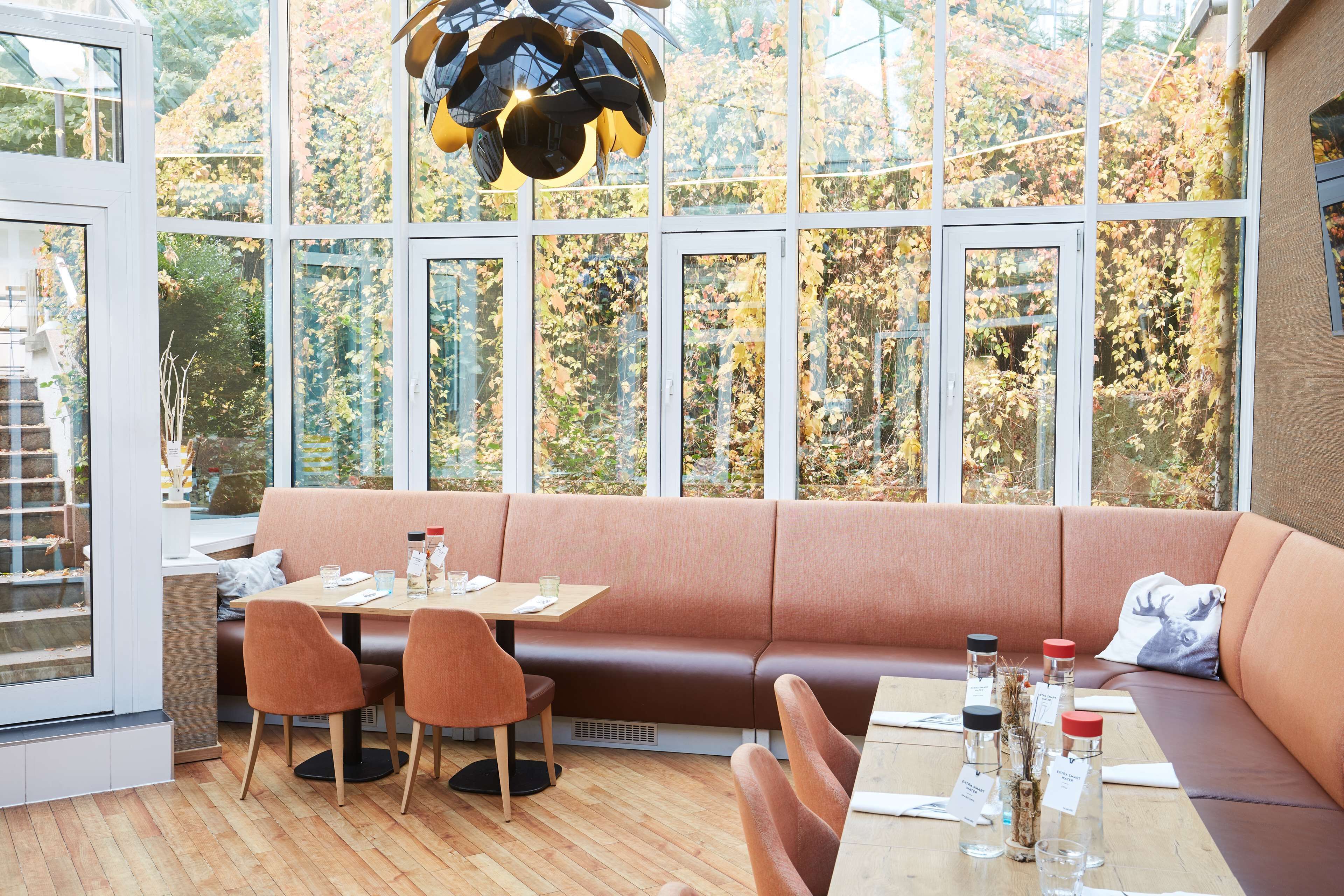 Un interior moderno con una mesa de madera, asientos acolchados marrones y ventanas amplias que dan a un paisaje de árboles.