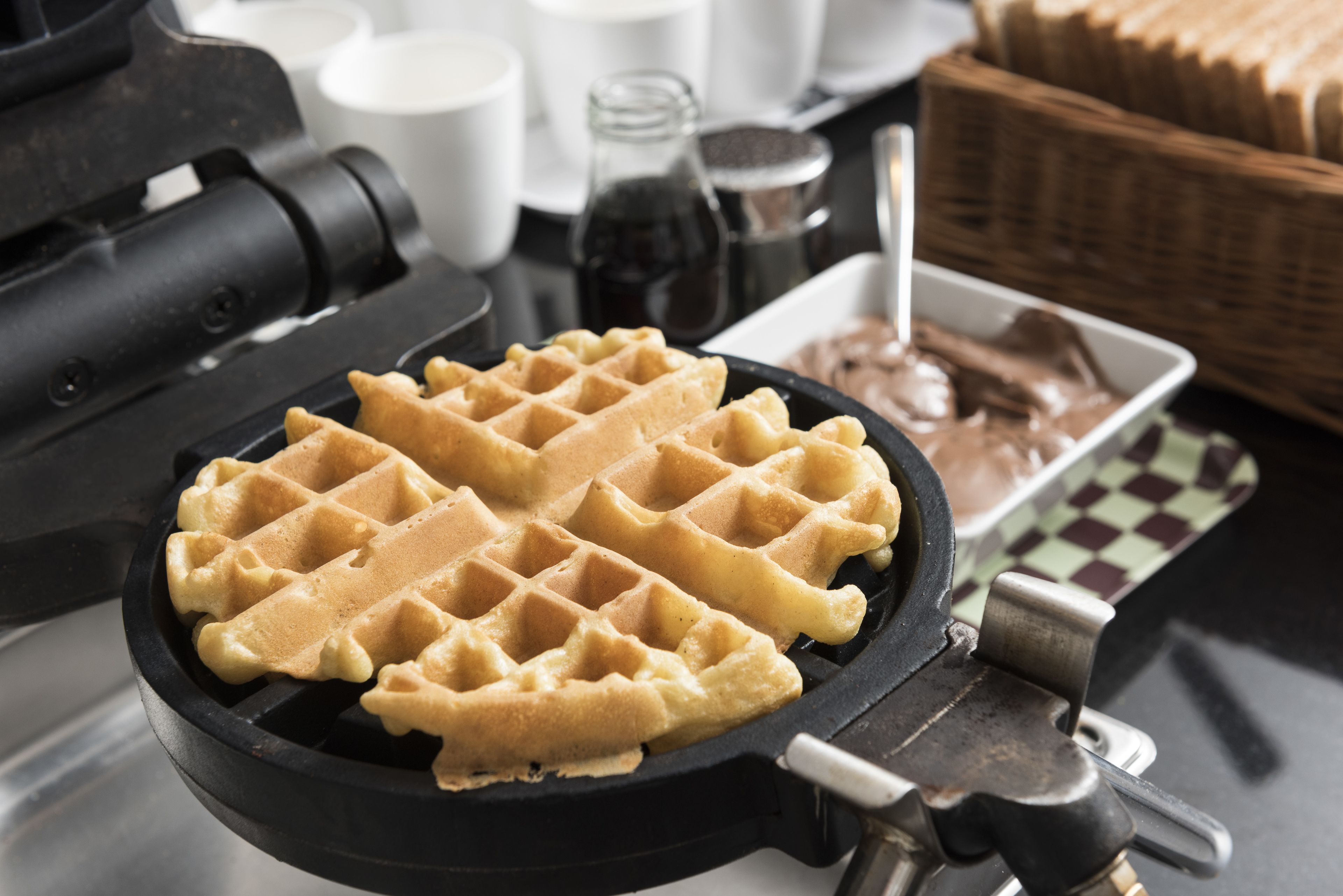 Un gaufrier avec des gaufres, un panier de pain et un pot de sauce au chocolat.