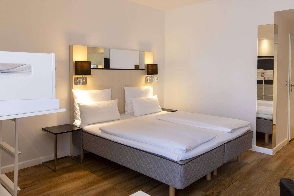A modern hotel room with a large bed, bedside tables, a mirror, and a wardrobe.