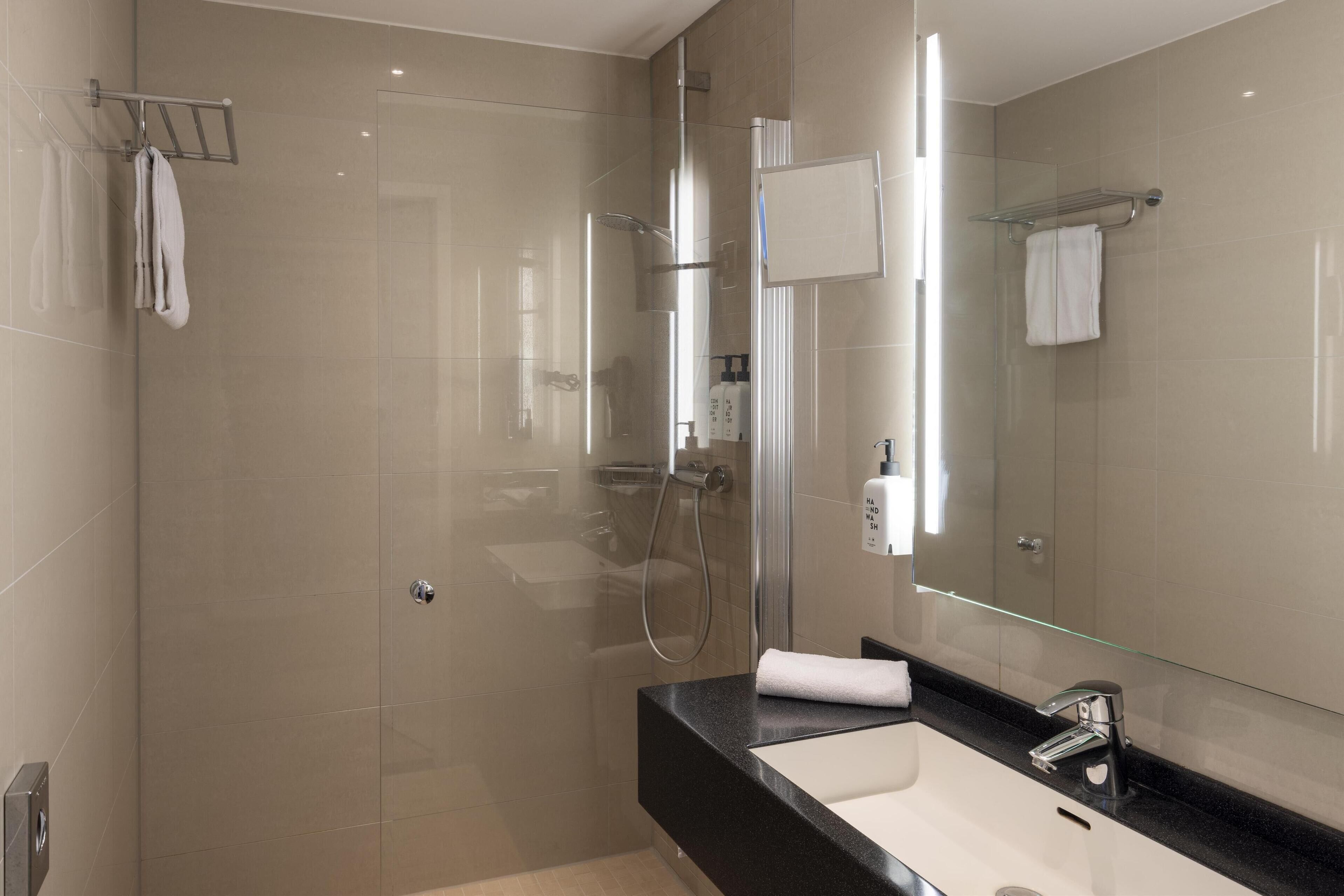 A modern bathroom with a glass-enclosed shower, a black countertop, and a large mirror.