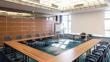 Un salón de conferencias con una gran mesa de madera, varias sillas, una pantalla de proyector y un amplio ventanal que proporciona luz natural.