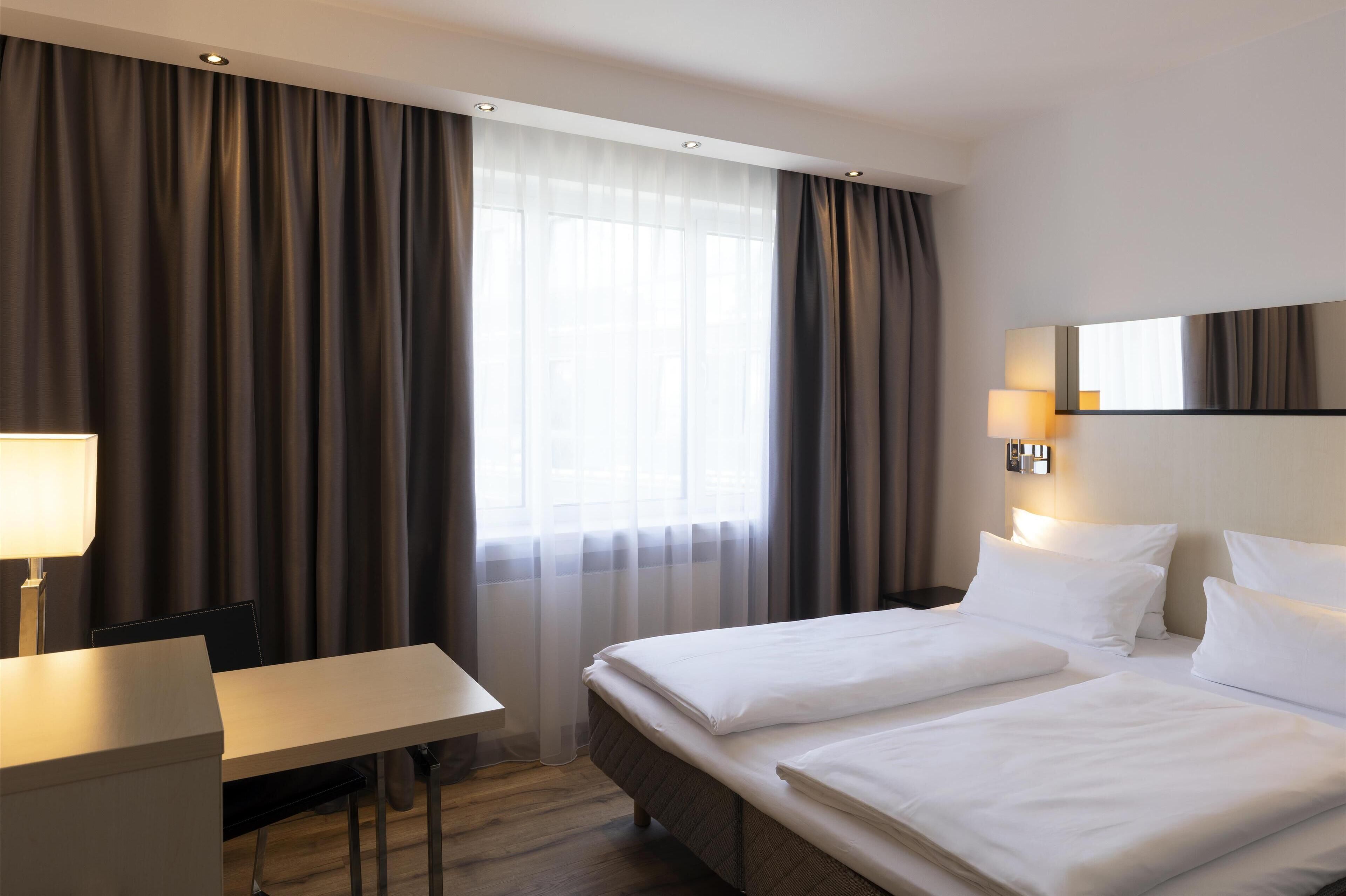 A hotel room with a bed, a desk, and a window with curtains.