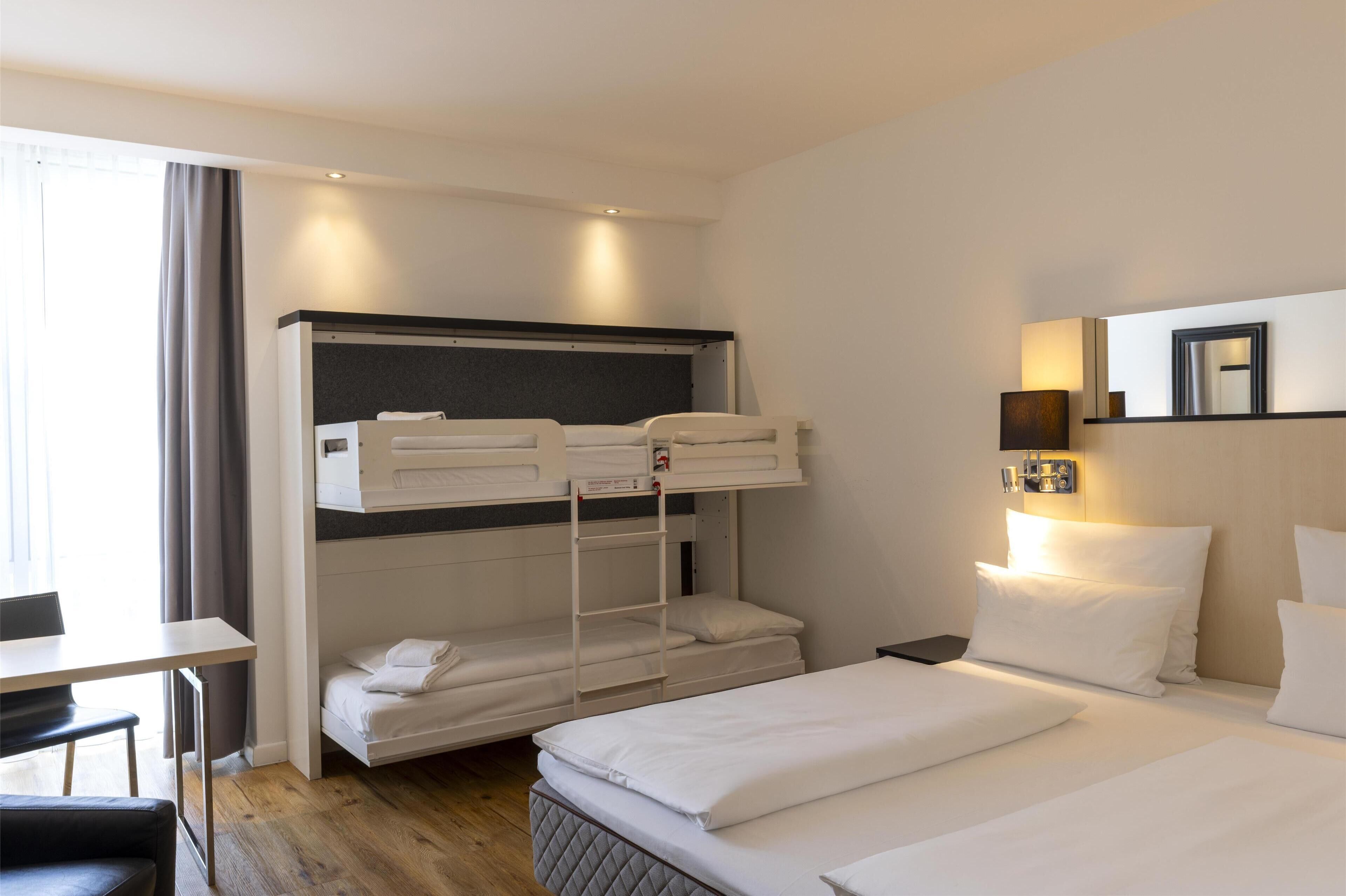Een hotelkamer met stapelbedden, een bureau, een stoel, een nachtkastje, een lamp en een spiegel.