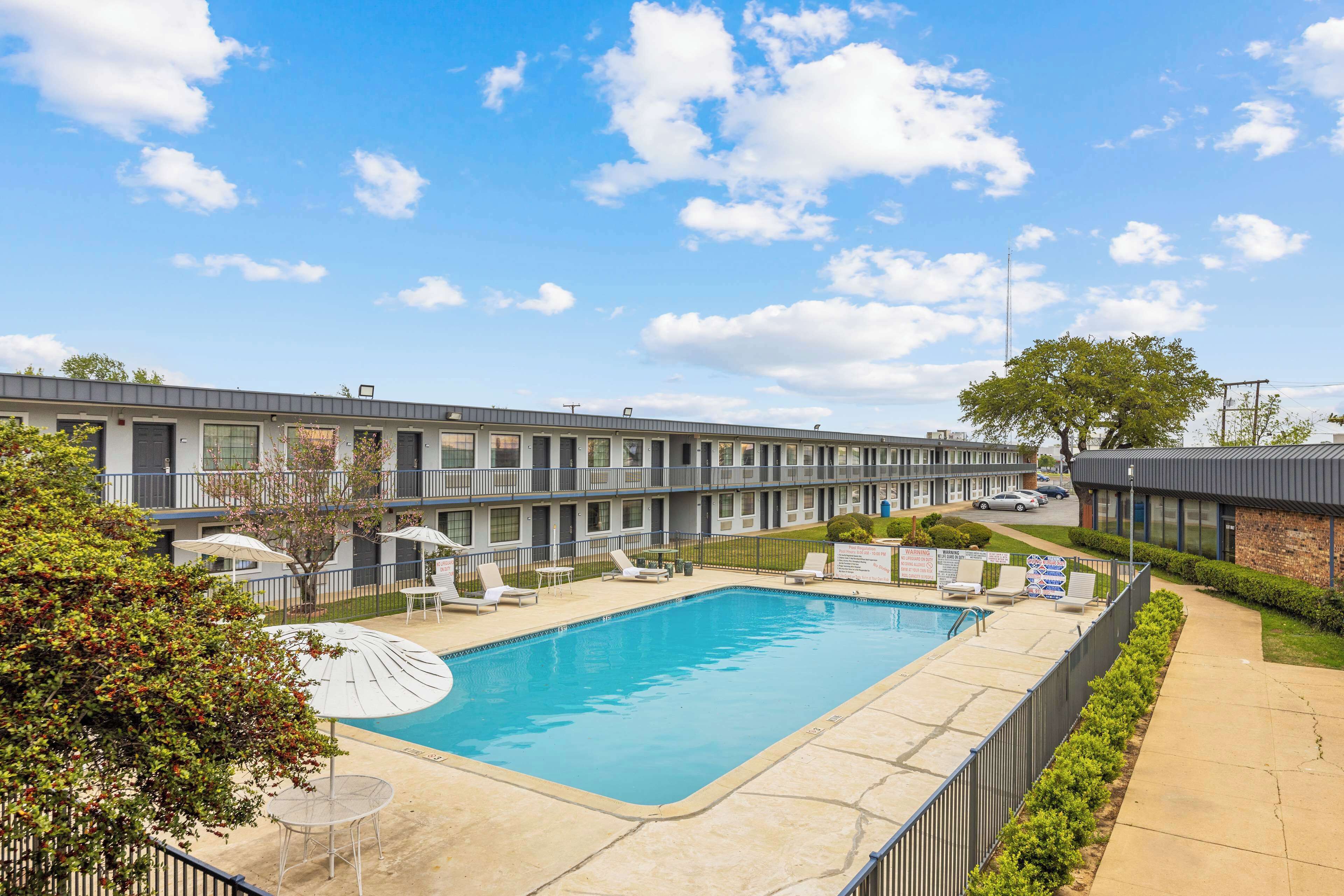 Um hotel com piscina, espreguiçadeiras e um pátio cercado.