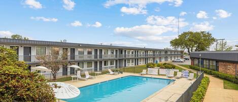 Um hotel com piscina, espreguiçadeiras e um pátio cercado.