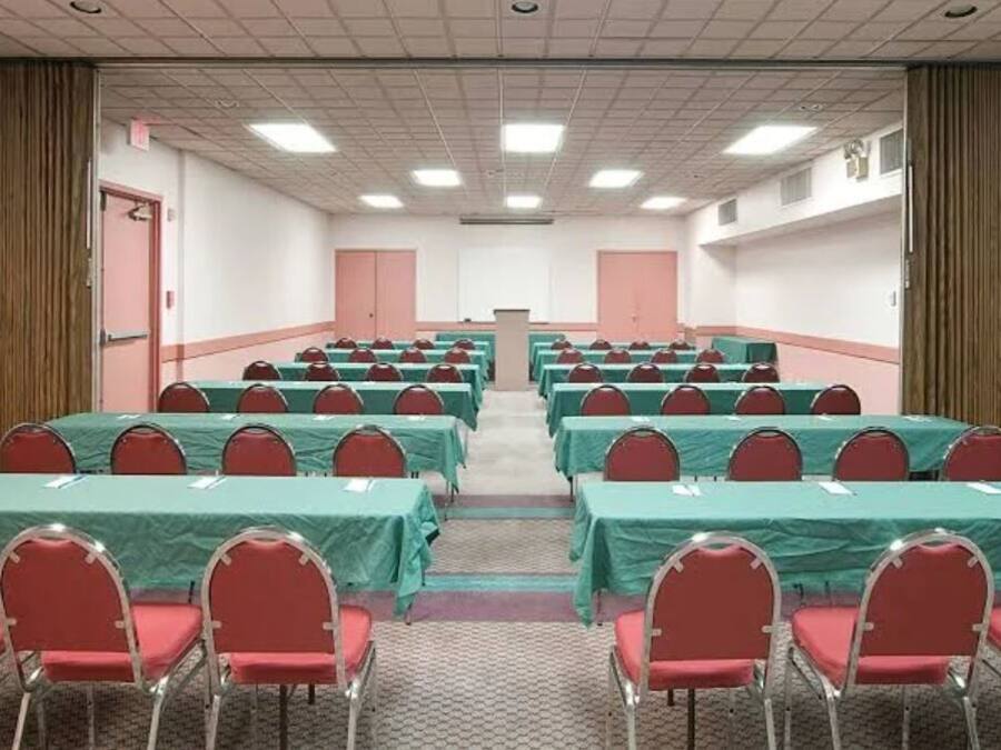 A conference room with rows of tables and chairs, a podium at the front, and curtains on the sides.