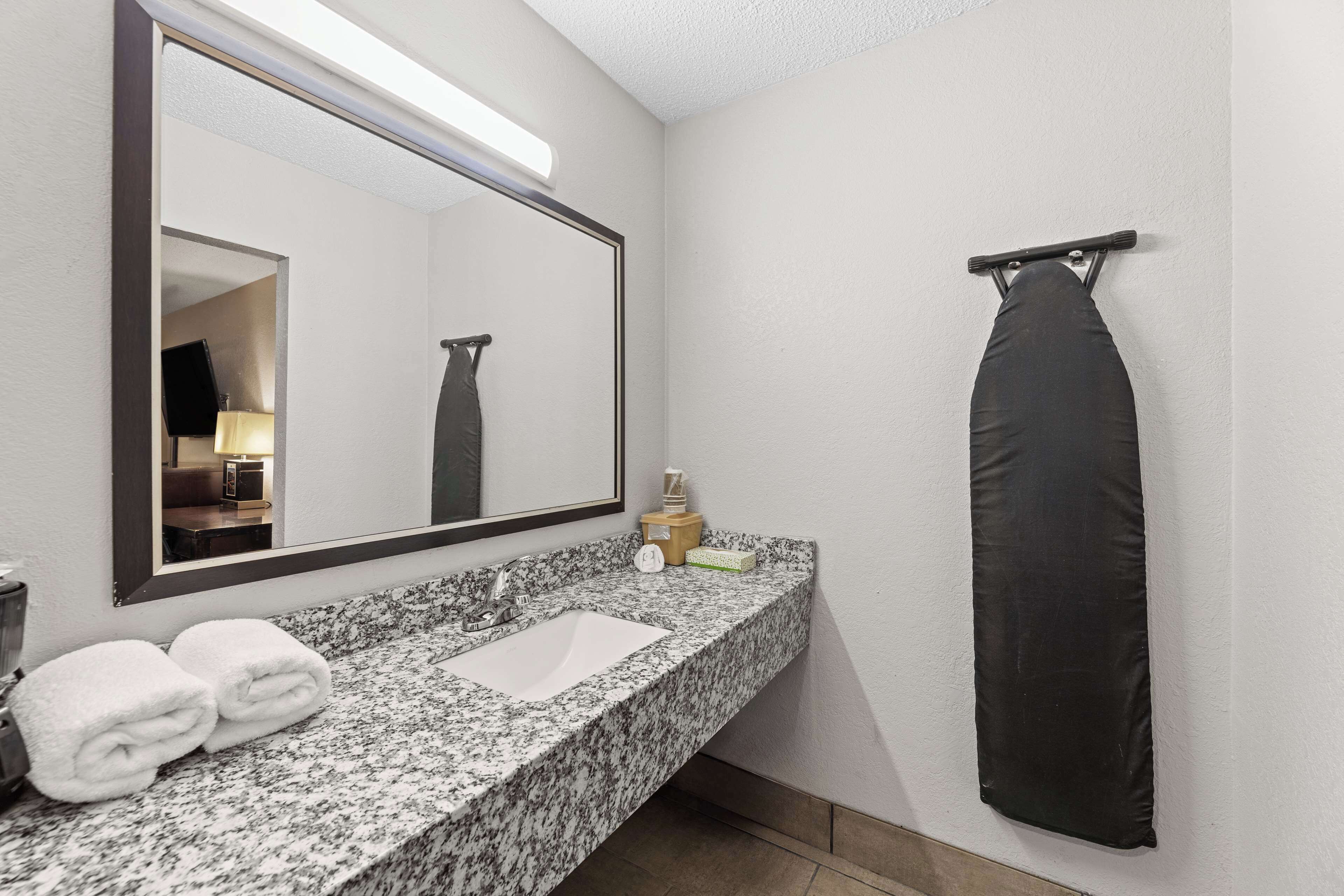 Une salle de bain dotée d’un comptoir en granit, d’un lavabo blanc, d’un grand miroir, d’un porte-serviettes noir et d’un présentoir à serviettes.