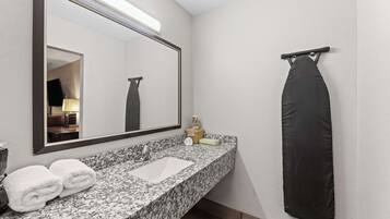 Une salle de bain dotée d’un comptoir en granit, d’un lavabo blanc, d’un grand miroir, d’un porte-serviettes noir et d’un présentoir à serviettes.