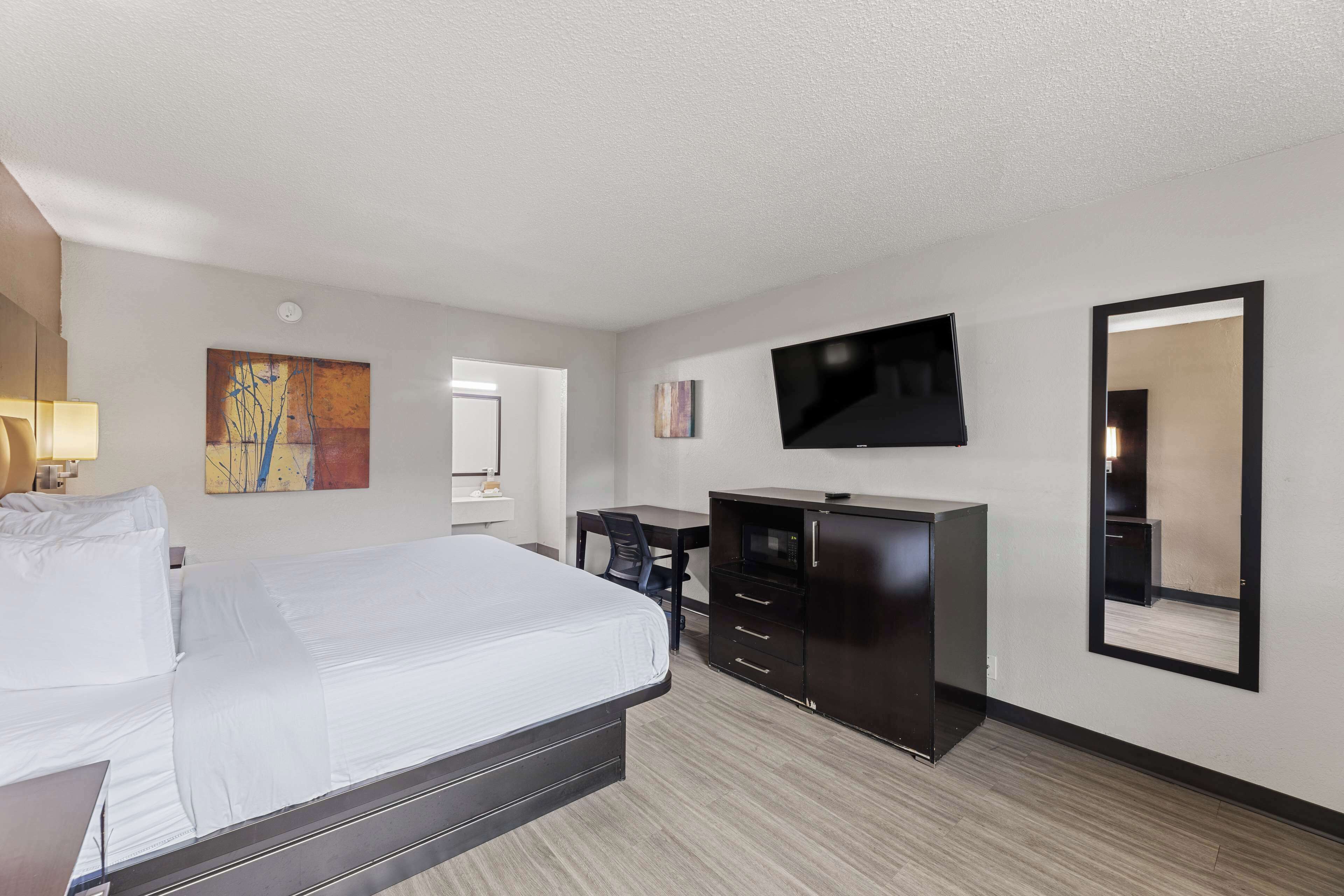 A hotel room with a large bed, a desk with a chair, a flat-screen TV mounted on the wall, and a dresser.