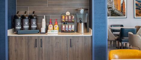 A hotel reception area with a coffee station, including coffee dispensers, a coffee machine, and a coffee menu.