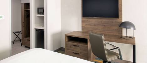 A hotel room with a bed, a desk with a chair, a television, and a wardrobe.