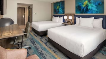 A hotel room with two beds, a desk, a chair, and a large abstract painting on the wall.
