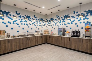 A modern breakfast area with a wooden counter, hexagonal wall decor, and various breakfast items. - La Quinta Inn & Suites by Wyndham Spokane Downtown (Spokane)
