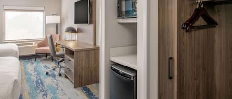 A hotel room with a bed, desk, chair, lamp, TV, microwave, and a wooden wardrobe.
