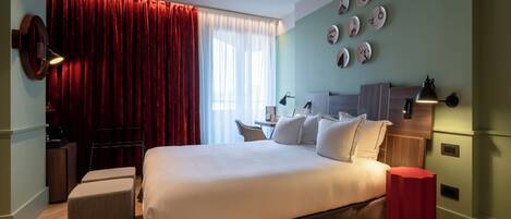 Habitación de hotel con una cama grande, un escritorio, una silla, una pared de acento roja y una ventana con cortinas.