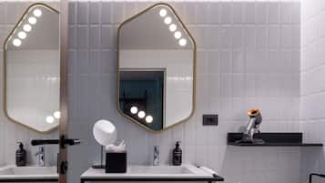 A modern bathroom with two sinks, a large mirror with lights, a towel rack, and a hairdryer on a shelf.
