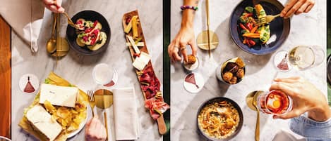 Un grupo de personas cenando en una mesa con varios platos, entre ellos un sándwich, una ensalada y una tabla de quesos.