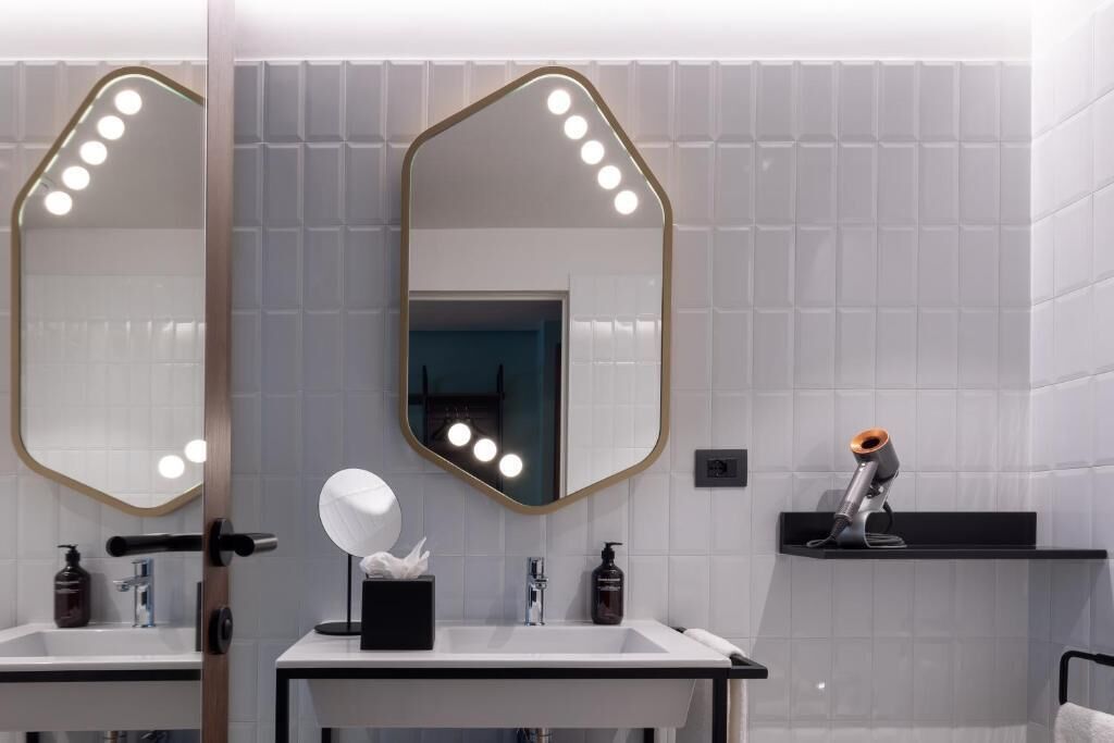 Une salle de bain moderne avec deux vasques, un grand miroir avec éclairage intégré et un sèche-cheveux posé sur une étagère.