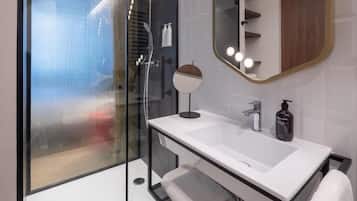 Een moderne badkamer met een douchecabine van glas, een witte wastafel met een ronde spiegel en een meubel met daaraan een handdoekhouder.