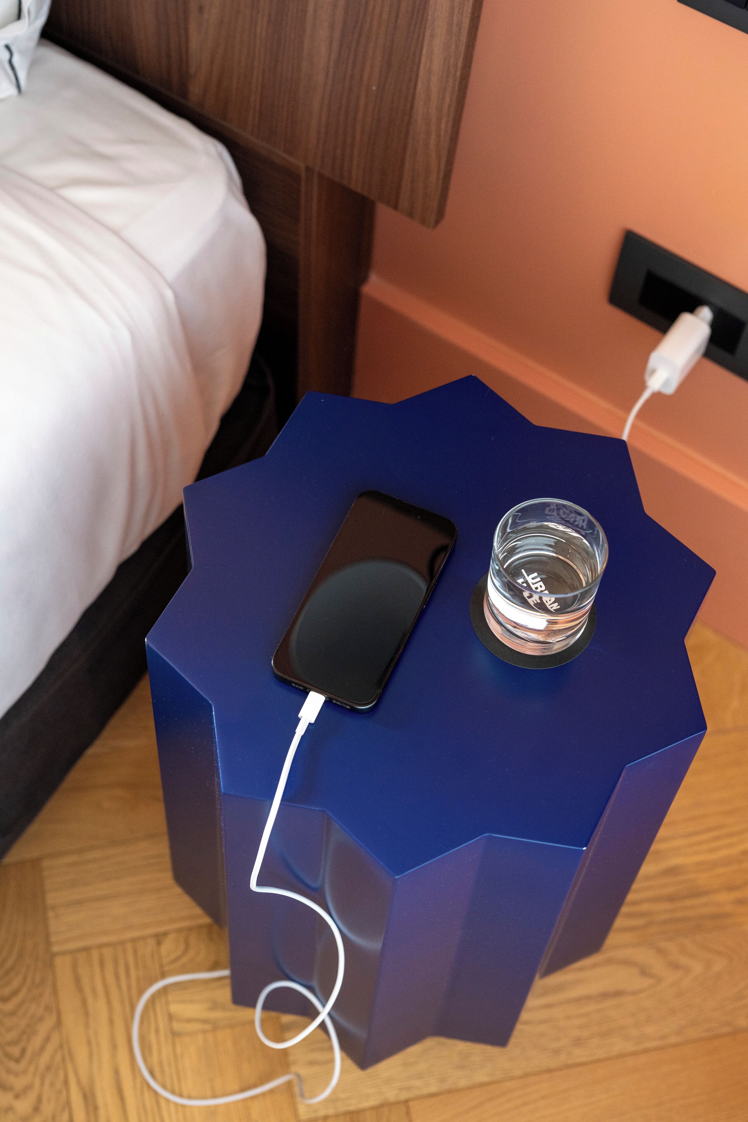 A smartphone on a blue octagonal charging dock with a glass of water beside it.