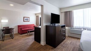 A hotel room with a flat-screen TV, a red sofa, a desk with chairs, and a large bed.