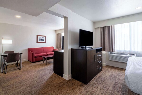 A hotel room with a flat-screen TV, a red sofa, a desk with chairs, and a large bed. - Best Western Pony Soldier Inn & Suites (Flagstaff)