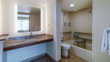 A bathroom with a sink, toilet, and bathtub, including a shower chair and grab bars.
