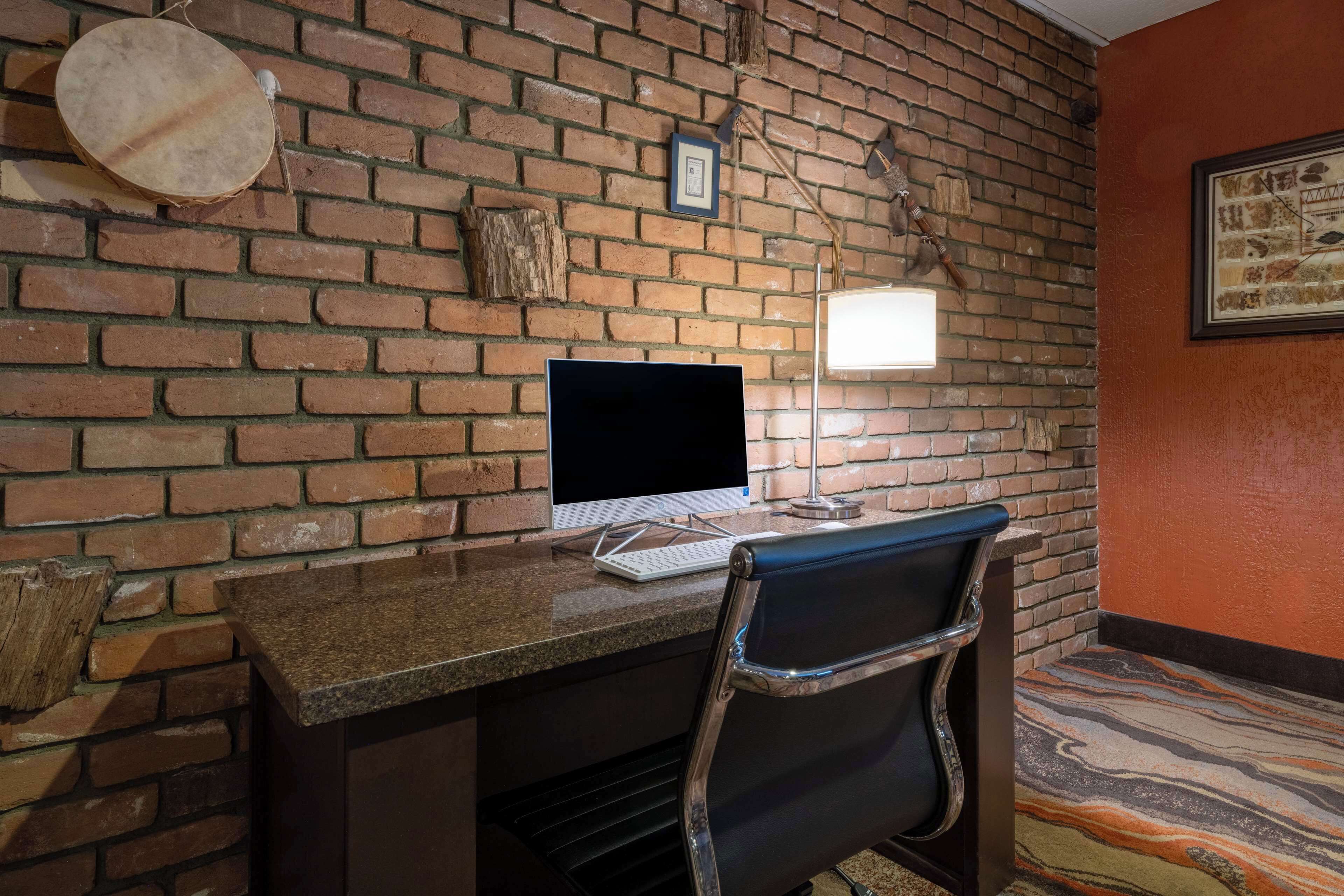 A brick-walled room with a desk, a computer, a chair, and a lamp.