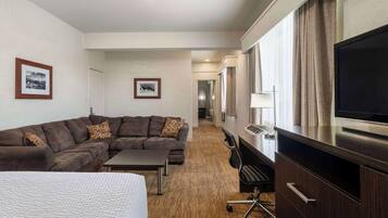 Habitación de hotel con una cama grande, un sofá marrón oscuro, una mesita, un televisor y un escritorio con cajones.
