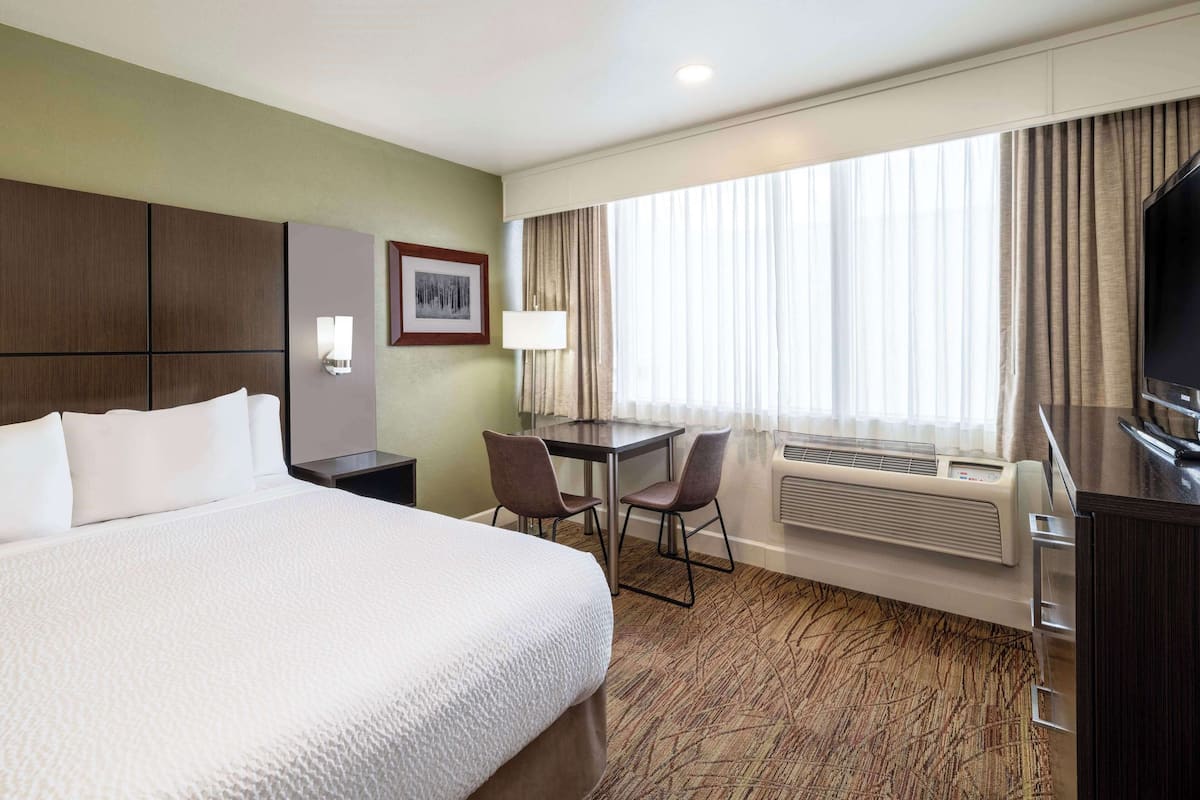 A hotel room with a large bed, a desk with two chairs, a television, and a window with curtains.
