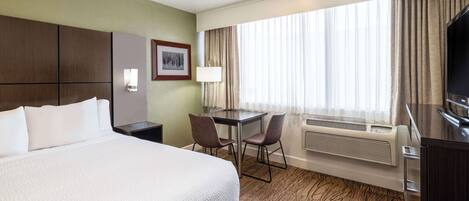 Habitación de hotel con una cama grande, un escritorio con dos sillas, un televisor y una ventana con cortinas.