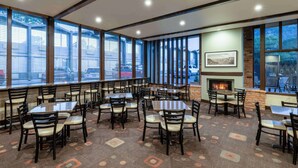 A spacious indoor dining area with multiple tables and chairs, large windows, a fireplace, and a view of the outside.