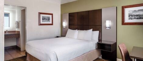 A hotel room with a large bed, a wooden headboard, a bedside table, a chair, and a small desk.