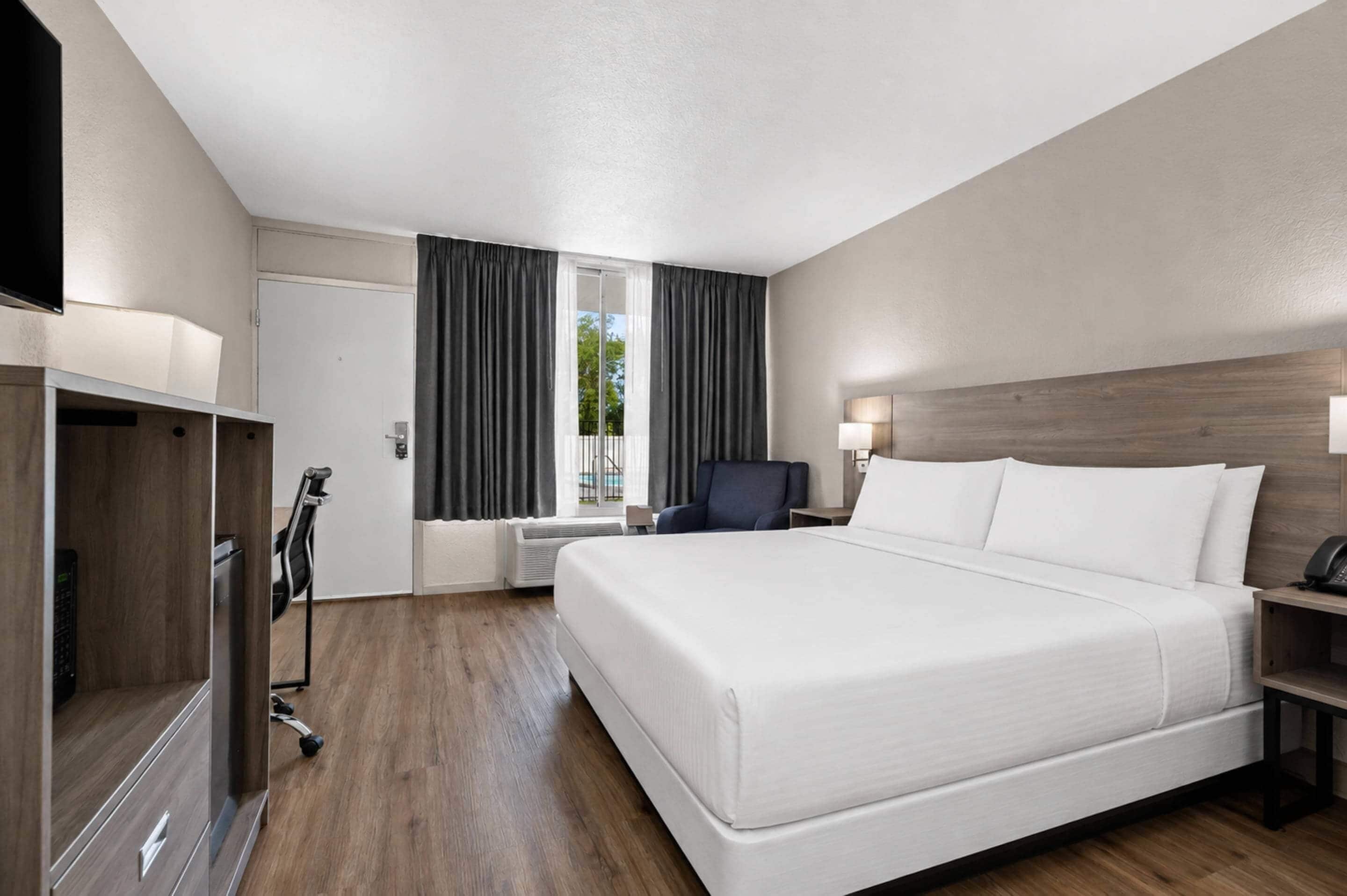 Une chambre d’hôtel avec un grand lit, un bureau avec une lampe, une chaise, une armoire et un téléviseur.
